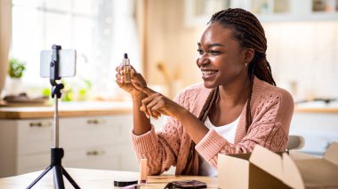 Neşeli Siyah Kadın Blogcu Evdeki Kozmetik Ürünleri İçin Görüntü İncelemesi Yapıyor, Gülümseyen Afrikalı Amerikalı Kadın Akıllı Telefon Kamerasında Yeni Cilt Serumu Gösteriyor, Mutfakta Masada Oturuyor