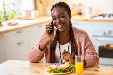 Neşeli Afro-Amerikan Kadın Lezzetli Kahvaltı Yiyor ve Mutfakta Cep Telefonuyla Konuşuyor, Arkadaşlarıyla Cep Telefonu Konuşan Mutlu Siyah Kadın ve Sağlıklı Lezzetli Yemekler, Bedava Alan