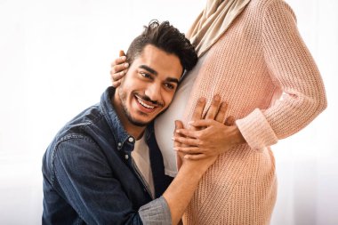 Mutlu doğu adamı hamile karısının karnını kucaklıyor, bebek tekmelerini dinliyor, Arap erkeği seviyor Müslüman eşinin karnına şefkatle dokunuyor, gelecekteki ebeveynliğinin tadını çıkarıyor, kırpılmış görüntüsü, yakın plan