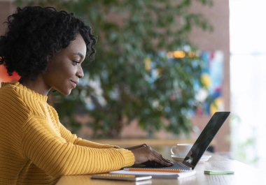 Kafede dizüstü bilgisayarda yazan siyah genç bayanın yan görüntüsü, internette çalışan, boş alan