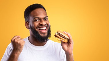 Elinde hamburgerle gezen neşeli siyah adam sağlıksız fast food yiyor sarı stüdyonun arkasında duruyor, kameraya gülümsüyor. Abur cubur aşığı. Son olarak Hile Yemeği