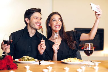 Capturing Moments. Beautiful lovely excited young couple taking selfie while sitting at table and having dinner. Smiling woman and man eating pasta, making photo, having fun at restaurant or at home