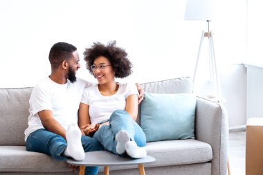 Yeni ev. İçeride taşınma gününün tadını çıkaran paketlenmiş kutuların arasında koltukta oturan mutlu siyah eşler. Gayrimenkul, Ev Sahipliği ve Kira Konsepti. Boşluğu Kopyala