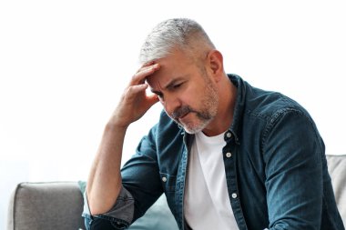 Üzgün, gri saçlı, evdeki koltukta oturan, ellerine yaslanıp bir şeyler düşünen, yan görüş, fotokopi alanı. Finansal veya sağlık sorunları olan yaşlı sakallı bir adam