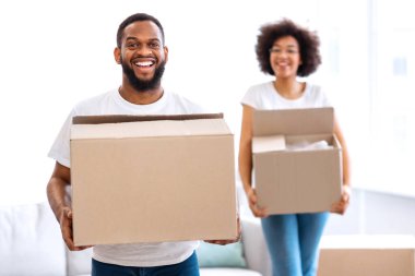 Neşeli Afrikalı bir çift taşınma kutularını yeni bir daireye taşıyor, kameraya gülümsüyor. Eşler kendi evine giriyor. Gayrimenkul, Genç Aile Konutları. Seçici Odaklanma