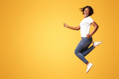 Turuncu stüdyo arka planında poz veren neşeli, genç siyah bir kadın, tam boy fotoğraf. Duygusal Afrikalı Amerikalı güzel bayan zıplıyor ve çığlık atıyor, mutluluk ve neşe gösteriyor.
