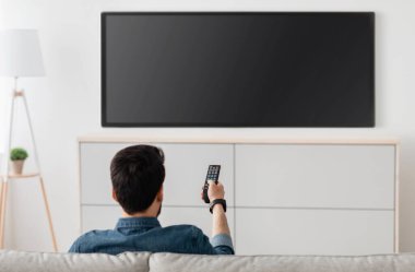 Adam televizyon izliyor, plazma düz ekran TV açıyor, beyaz duvardaki boş TV ekranına uzaktan kumanda doğrultuyor. Adam evde kanal değiştiriyor, arkadan bakıyor. Model