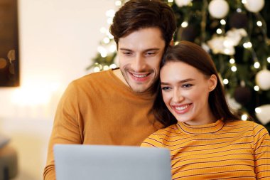 People And Technology. Portrait Of Smiling Beautiful Couple Holding And Using Laptop Pc Sitting On Couch Indoors In Living Room. Happy Family Surfing Internet Choosing Gift, Watching Movie Online