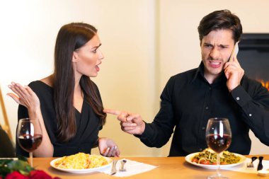 İlişki Sorunu ve Çatışmalar. Sinirli bir kadın akıllı telefonuyla konuşan ve lokantada randevusu varken parmağını gösterip bekleyen erkeğine bakıp bağırıyor.