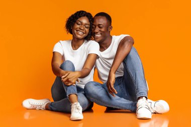 Siyahi erkek ve kadını sevmek, yerde oturmak, gözleri kapalı gülmek, stüdyo çekimi, turuncu arka plan, fotokopi alanı. Aşk, aile, ilişkiler, arkadaşlık, evlilik kavramı