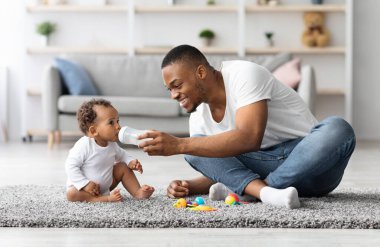 Genç siyah bir babanın evde bebeğine su şişesi vermesi, Afrikalı bir Amerikalının babasını sevmesi, sevimli bir çocuğa bakıcılık yapması, oturma odasında yerde birlikte oynaması.