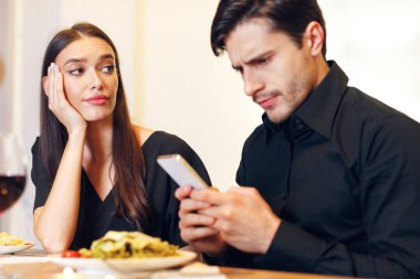 Bad Date. Unhappy Sad Beautiful Woman Is Getting Bored Sitting On Date Event In Restaurant While Her Boyfriend Using Mobile Phone And Chatting, Ignoring His Girlfriend. Relationship Problem Concept
