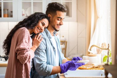 Genç Arap koca öğle yemeğinden sonra bulaşıkları yıkıyor, karısına ev işlerinde yardım ediyor. Orta Doğulu Aile Mutfakta Yemek yedikten sonra Temizlik, Minnettar Kadın Kocaya Sarılma, Boş Alan