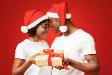 Noel Baba şapkalı Afrikalı Amerikalı aşıklar yeni yıl kutlamalarında sihirli anlar yaşıyorlar. Alınlarıyla birbirlerine dokunuyorlar ve gülümsüyorlar. Hediye tutuyorlar.