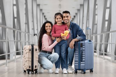 Mutlu Arap anne, baba ve küçük kızı birlikte havalimanında poz veriyorlar, genç orta doğulu ebeveynler ve bavulları olan şirin bir bayan çocuk Terminal Salonu 'nda uçuşu bekliyor, boş alan.