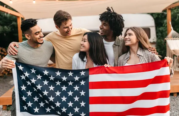 Milenyum ırkları arası arkadaşlar ellerinde Amerikan bayrağı ve karavanın önünde gülümsüyorlar. Ulusal Bağımsızlık Günü 'nü dışarıda kutlayan çok uluslu gençler.