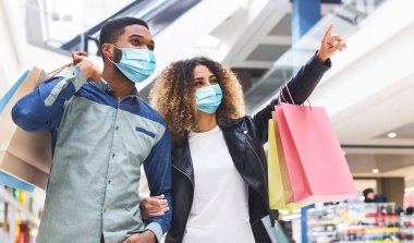 Karantina sırasında alışveriş. Genç Afro-Amerikan çift alışveriş merkezinde birlikte alışveriş yapıyorlar koruyucu maskeler takıyorlar, panorama. Siyahi kadın erkek arkadaşına yeni mağazasını gösteriyor.