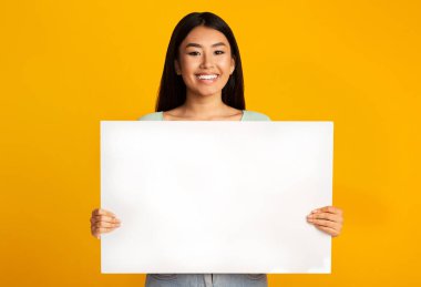 Gülümseyen Asyalı Kadın Boş Beyaz Poster İlan Veriyor Sarı Stüdyo Arkaplanında Bir Şey Duruyor. Model