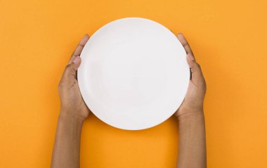 Öğle yemeği vakti. Turuncu arka plan üzerinde boş plaka tutan siyah kadın elleri, üst görünüm, boş alan