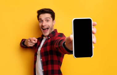 Mobil Uygulama Reklamı. Yakışıklı Heyecanlı Adam, Siyah Boş Cep Telefonu Ekran Görüntüsü Sarı Stüdyo Arkaplan Görüntüleme Cihazı Kameraya Yakın. Bu Gadget Çıkış 'ı Kontrol Et, Görüntüle Modifiye Et