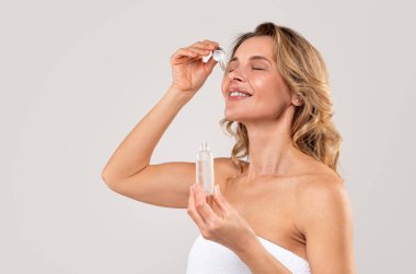 Yaşlanma karşıtı rutin. Açık gri stüdyo arkaplanına sarılı vaziyette dururken Düşüren Güzel Orta Çağ Kadınları Nemlendirici Cilt, Boş Alan