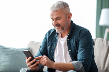 Gülümseyen son sınıf öğrencisi evde dinlenirken akıllı telefon kullanıyor, online çöpçatanlık hizmeti kullanıyor, fotokopi çekiyor. Neşeli, yaşlı, sakallı adam. Mobil uygulamanın keyfini çıkarıyor. Oturma odasının içini.