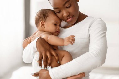 Doğum Konsepti. Afrika kökenli Amerikalı bir annenin üzgün bebeğini kucaklayıp tuttuğunun portresi. Mutlu olmayan aç bir bebek, sızlanıyor, acı çekiyor ya da sancı çekiyor. Boşluğu kopyala, arkaplanı bulanıklaştır