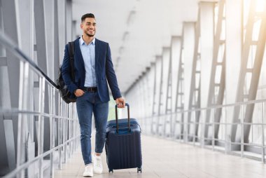 Yolculuk için hazır. Havalimanı Terminali 'nde bavulla dolaşan yakışıklı bir Arap, uçuş kapısına giderken yanında bavulunu taşıyan gülümseyen genç bir Orta Doğulu.