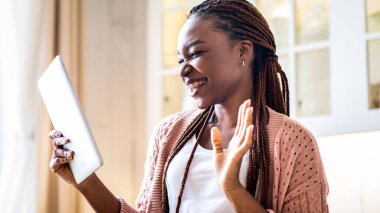 Mutfakta dijital tabletle video görüşmesi yapan neşeli siyah kadın, kameraya el sallayan Afrikalı Amerikalı genç bayan, çevrimiçi iletişimin keyfini çıkartıyor,