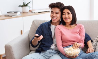 Çinli bir çift hafta sonu televizyon seyrediyor, patlamış mısır yiyor uzaktan kumandayla televizyon kanallarını değiştiriyor evdeki oturma odasında koltukta oturuyor..