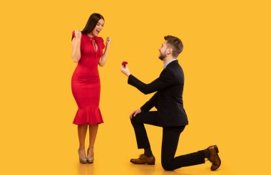 Evet dedi. Erkek Kız Arkadaşına Yüzüğünü Kutuda Teklif Ediyor Stüdyoda Diz çökmüş Sarı Arkaplanda