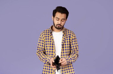 Ekonomik kriz konsepti. Mutsuz Hintli adam menekşe arka planda boş cüzdana bakıyor.