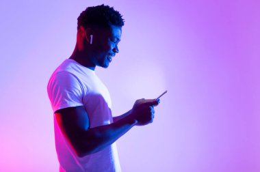 Çevrimiçi yaşam konsepti. Milenyum siyahi adam cep telefonu kullanıyor, internet ya da sosyal medyayı neon ışıkta kontrol ediyor, kopyalama alanı kullanıyor. Havalı Afrikalı Amerikalı adam elinde modern bir alet tutuyor, internette mesajlaşıyor.