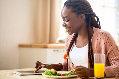 Gülümseyen Siyah Kadın Mutfakta Kahvaltı Yaparken Dijital Tablet Kullanıyor, Afro-Amerikalı Neşeli Kadın İnternetten Alışveriş Yapıyor veya Sosyal ağları kontrol ediyor