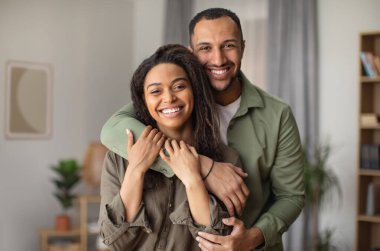 Mutlu evlilikler. Neşeli Afrikalı Amerikalı koca, karısına sarılıyor ve gülümsüyor. Kameraya bakıyor. Birlikte poz veren mutlu çift. Aşk ve Romantik İlişki Konsepti