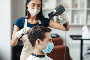 Önleyici önlemler. Kuaförde maskeli müşterinin saçını kurutma ustası, kapat.