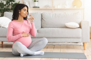 Eğitimden sonra evde su içen genç zenci hamile kadın fotokopi odasına bakıyor.