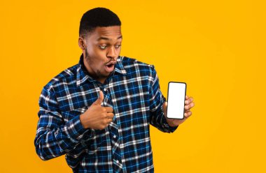 Harika Mobil Uygulama. Akıllı Telefon Gösteren Afrikalı Adam Boş Ekran Hareketi Başparmaklarını Sarı Arkaplan Üzerine Kaldırıyor. Stüdyo Çekimi, Model