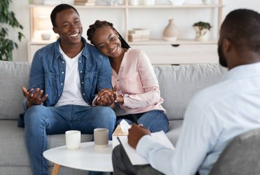 Aile danışmanlığı. Psikoterapistlerin ofisinde oturan genç mutlu siyah çift başarılı bir uzlaşmadan sonra el ele tutuşuyor Afrikalı eşler kurtarılan evliliğin danışmanına minnettarlar.