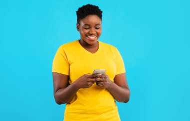 Gülümseyen Siyah Büyük Bayan Akıllı Telefon Mesajı Kullanıyor Mavi Stüdyo Arkaplanının Üzerinde Duruyor. Gezici Uygulama Kullanan Afrikalı Milenyum Kadını. Mutlu Kadın Telefon Kullanıcı Konsepti