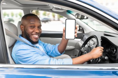 Lüks bir arabada oturan neşeli genç siyah adam, cep telefonunu beyaz ekranlı gösteriyor, navigasyon için en yeni mobil uygulamayı öneriyor, maket. Otomobil, sürüş ve modern teknolojiler