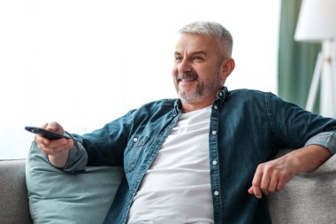 Mutlu sakallı son sınıf öğrencisi evdeki kanepede dinleniyor, uzaktan kumanda tutuyor, televizyon izliyor, fotokopi çekiyor. Oturma odasında kanepede dinlenen rahat olgun bir adam TV dizisi ya da dizi izliyor.