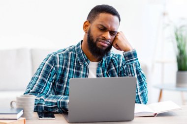 Sıkıcı siyahi adam laptopta oturuyor ve sıkıcı işinden nefret ediyor. Modern ofiste iş gününden sonra yoruldu. İşyerindeki Burnout. İş ve Girişimcilik Sorunu Kavramı