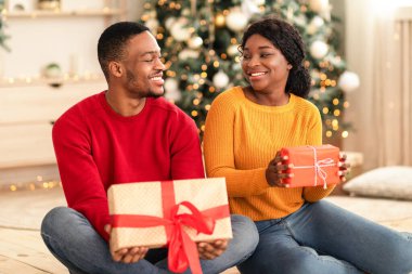 Yılbaşı havası ve Noel ağacının yanındaki evde hediye alışverişi. Milenyum mutlu Afro-Amerikan ailesi yere oturup birbirlerine bakıyorlar ve içinde çelenkler olan hediyeler olan kutuları tutuyorlar.