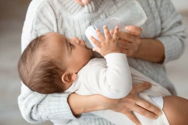 Bebek Bakımı ve Bebek Besleme Konsepti. Tanımlanamayan bir kadının elinde küçük tatlı bir Afrikalı Amerikalı bebeği tutması, elinde süt şişesi tutması, su içen çocuk.