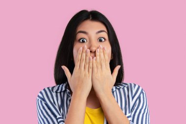 Tüh. Şaşırmış genç Asyalı kadının yakından çekilmiş portresi kameraya bakıyor ve elleriyle ağzını kapatıyor, haber ya da teklif karşısında şoka uğruyor, pembe stüdyo arka planında tek başına duruyor, afiş.