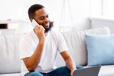 İçerideki koltukta oturup dizüstü bilgisayarda çalışırken cep telefonuyla konuşan neşeli, Kara Serbest Çalışan Adam. Uzak Mobil İletişim, Uzak Görev ve Serbest Kariyer Konsepti