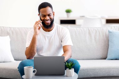 Her zaman temastayız. Dizüstü bilgisayarda çalışan Afrikalı bir adam ve evde koltukta oturup uzaktan iş görüşmesi yapan bir telefon var. Serbest Kariyer ve Uzak Mobil İletişim. Boşluğu Kopyala