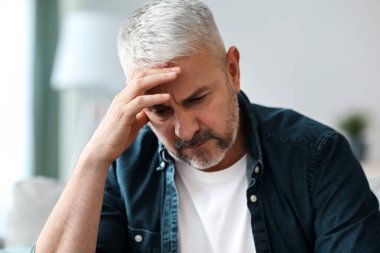 Hüsrana uğramış kıdemli sakallı bir adam evdeki kanepede oturuyor, kafasına dokunuyor, maddi sorunları var ya da baş ağrısı çekiyor, yakın plan, kopyalama alanı.