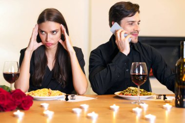 Bad Date. Unhappy Sad Desperate Woman Is Getting Bored Sitting On Date In Restaurant While Her Young Smiling Boyfriend Talking On Mobile Phone, Ignoring His Girlfriend. Relationship Problem Concept